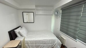 A compact room with a bed, a desk, a chair, a small table, a bench, a mirror, and a window with blinds. - Simple but cozy, feel at home (Mandaluyong City)
