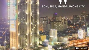 A high-rise building with multiple floors, large windows, and a prominent illuminated sign on the side. - Simple but cozy, feel at home (Mandaluyong City)