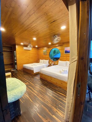 A wooden cabin-style room with two beds, a round mirror, and a ceiling fan.