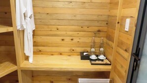 Un sauna de madera con un banco, un perchero para toallas y una pequeña mesa con botellas y vasos.