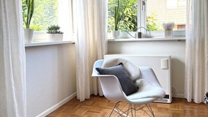 A modern room with a white chair, a rocking chair, and a view of greenery outside through large windows. - Vacation apartment "Badener18" with terrace (Offenburg)