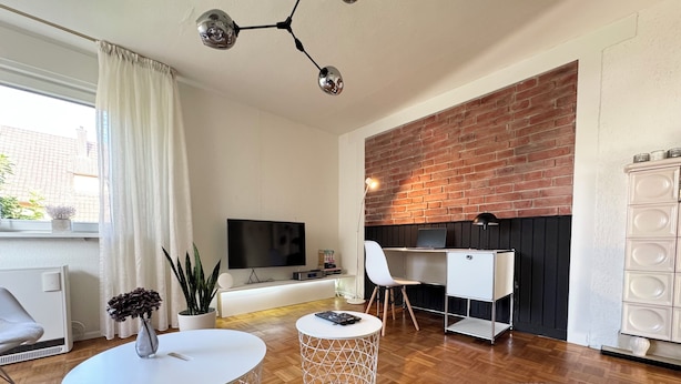 A modern living room with a TV, a desk, and a comfortable seating area. - Vacation apartment "Badener18" with terrace (Offenburg)