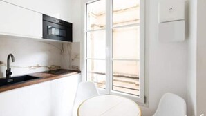 A modern kitchen with a black sink, white cabinets, and a window with blinds. - Apt Tour Eiffel invalides (Paris)