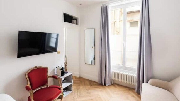 A modern living room with a flat-screen TV, a red chair, a sofa, and a large window with curtains. - Apt Tour Eiffel invalides (Paris)