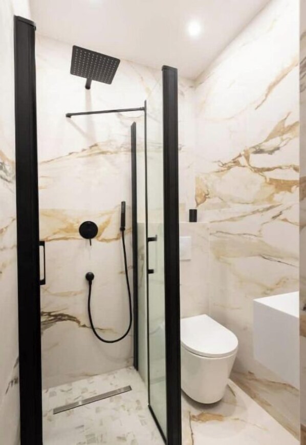 A modern bathroom with a glass-enclosed shower, a white toilet, and marble walls.