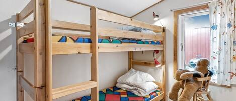 A bunk bed with a colorful geometric-patterned mattress, a small desk with a lamp, and a teddy bear on a chair.