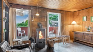 A cozy living room with a wood-paneled ceiling, a fireplace, leather sofa, and a dining area with chairs.