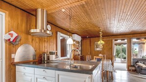 A modern kitchen with wooden paneling, a large island with a sink, and a dining area with a view.
