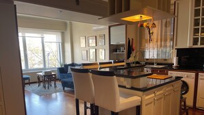 Una cocina moderna con una isla central, taburetes de bar y un área de comedor con sofá y sillas.