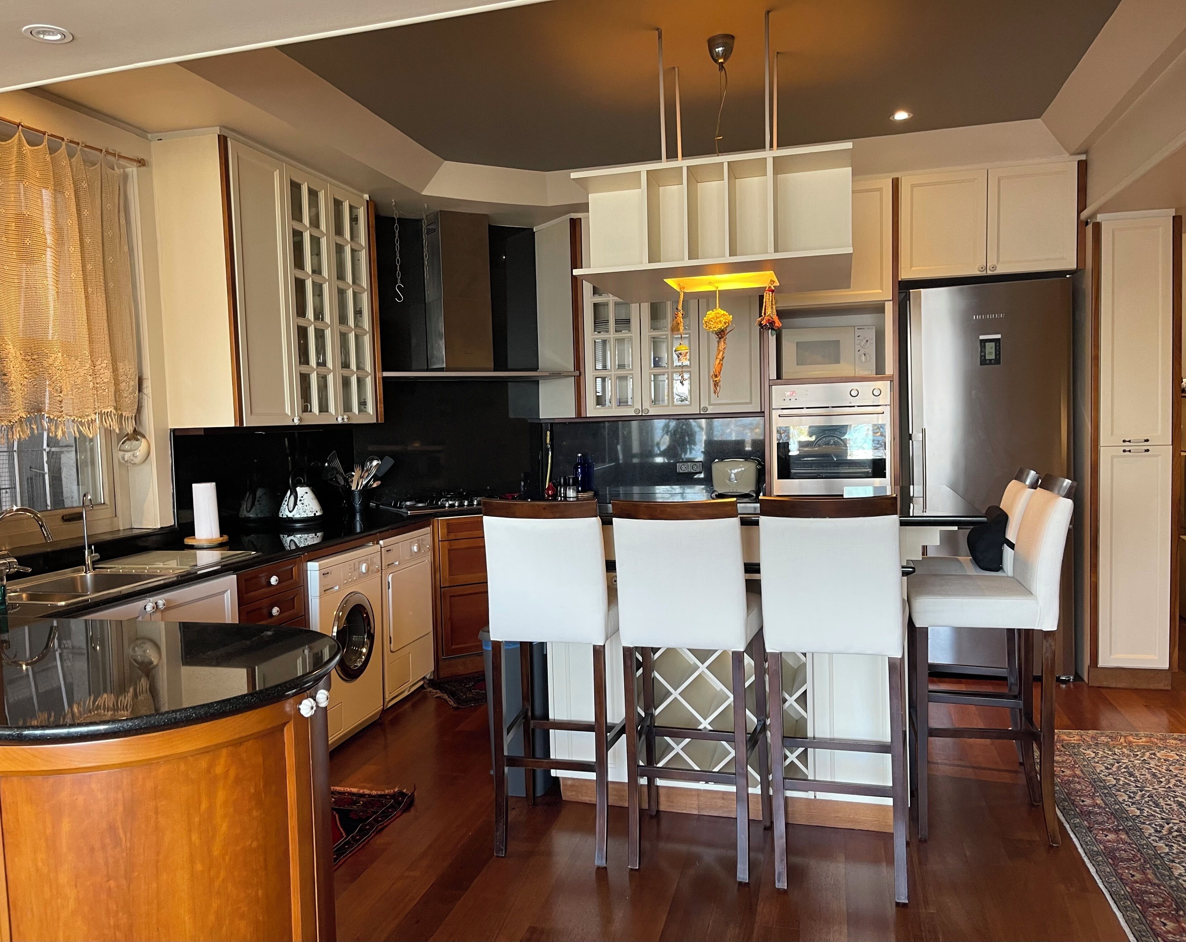 A modern kitchen with a central island, bar stools, a microwave, and a refrigerator.