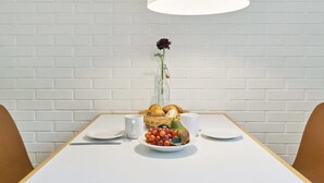 A dining table with a white tablecloth, a white pendant light, a vase with a single flower, and a basket of bread and fruit. - "Bengta" - 250m from the sea by Interhome (Nexø)