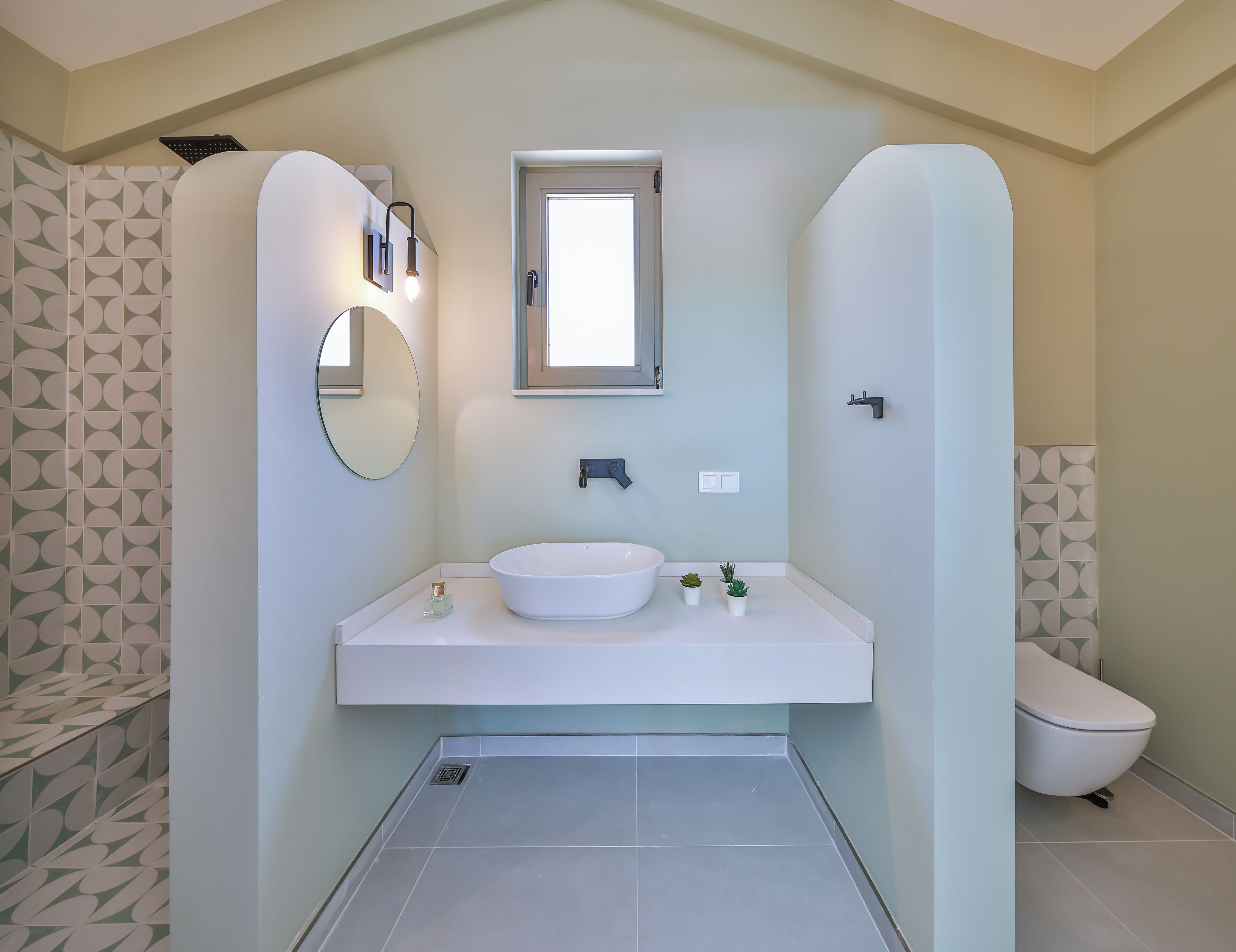 A modern bathroom with a large white sink, a round mirror, and a toilet.