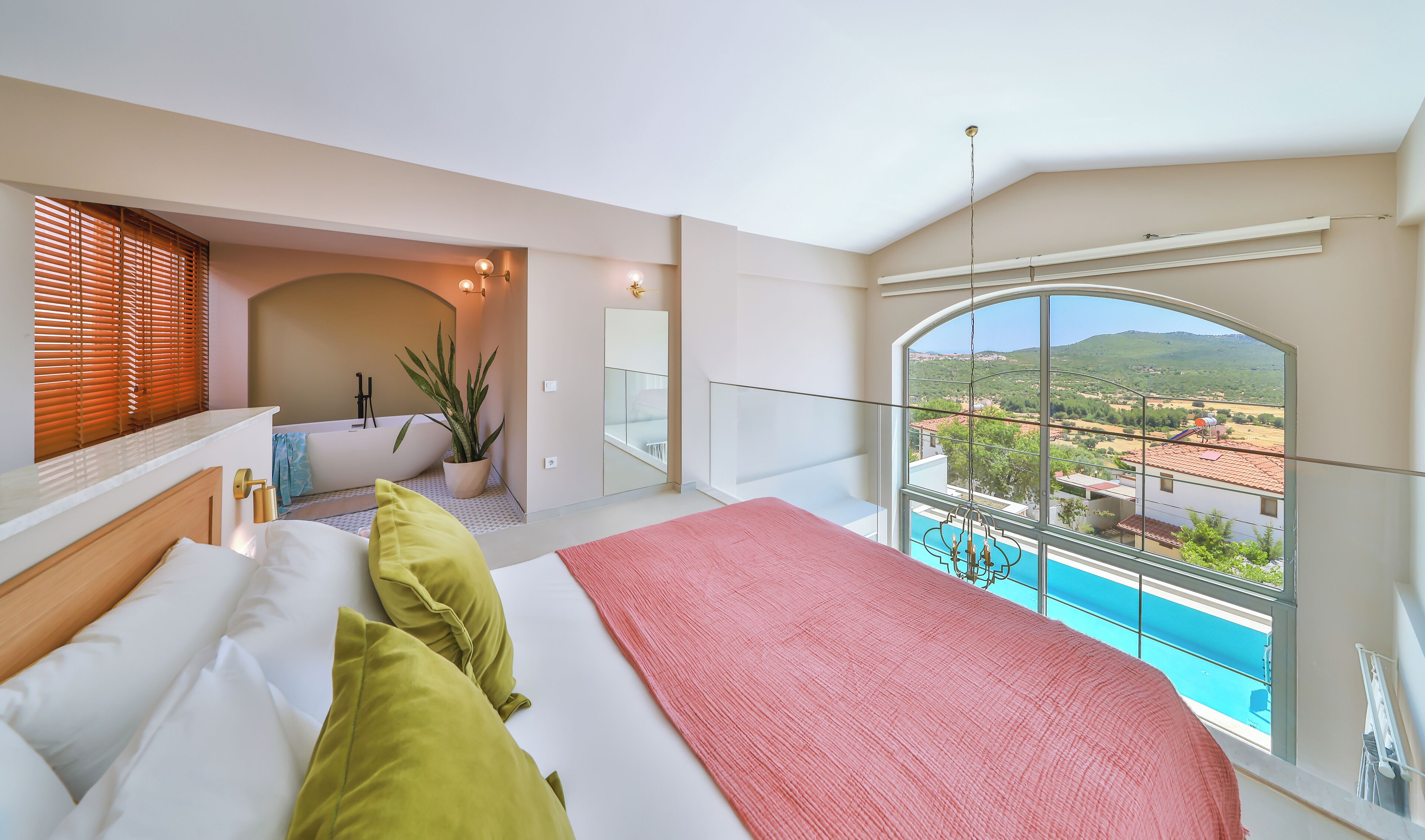 A bedroom with a large bed, a view of a pool, and a balcony with a view of the countryside.