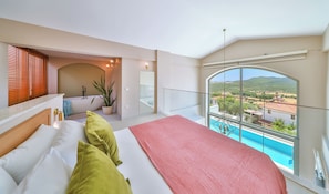 A bedroom with a large bed, a view of a pool, and a balcony with a view of the countryside.