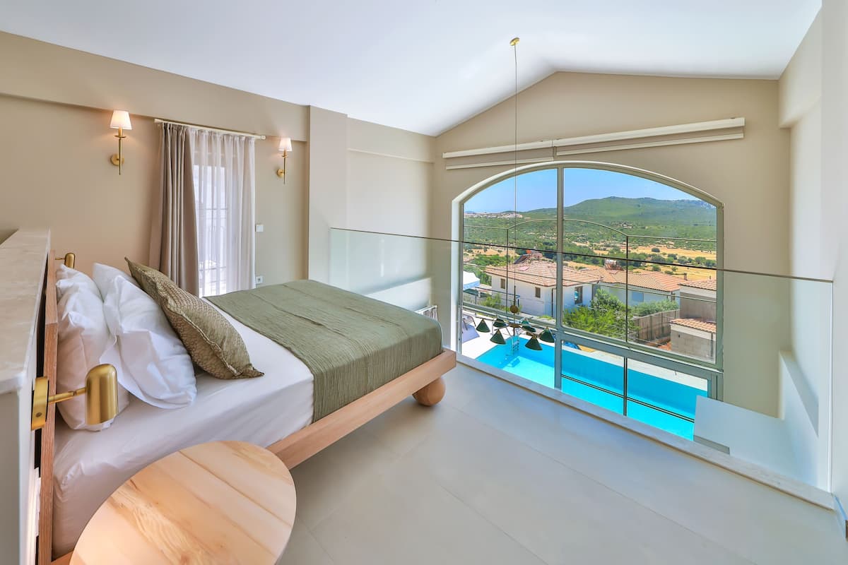 A bedroom with a bed, a view of a swimming pool, and a balcony with a glass railing.