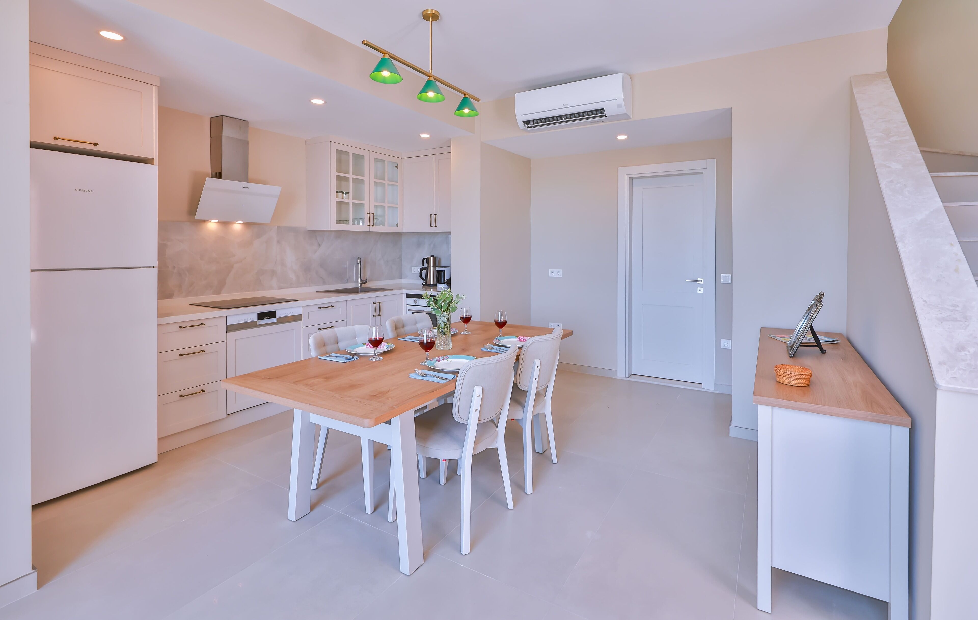 Una cocina moderna con armarios blancos, una mesa de comedor de madera y una pequeña mesita auxiliar.