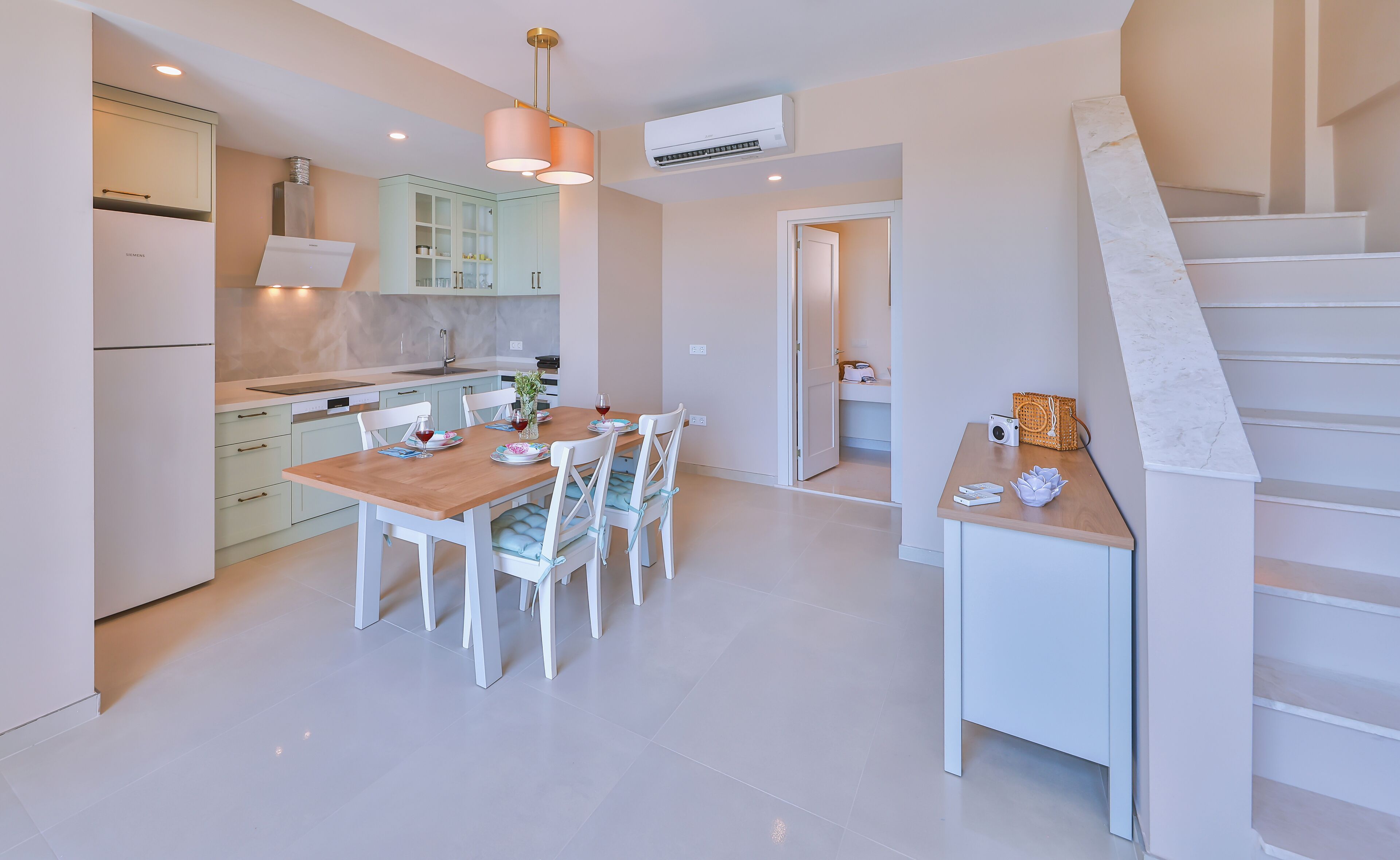 A modern kitchen with white cabinets, a dining table set for four, and a staircase leading to an upper level.
