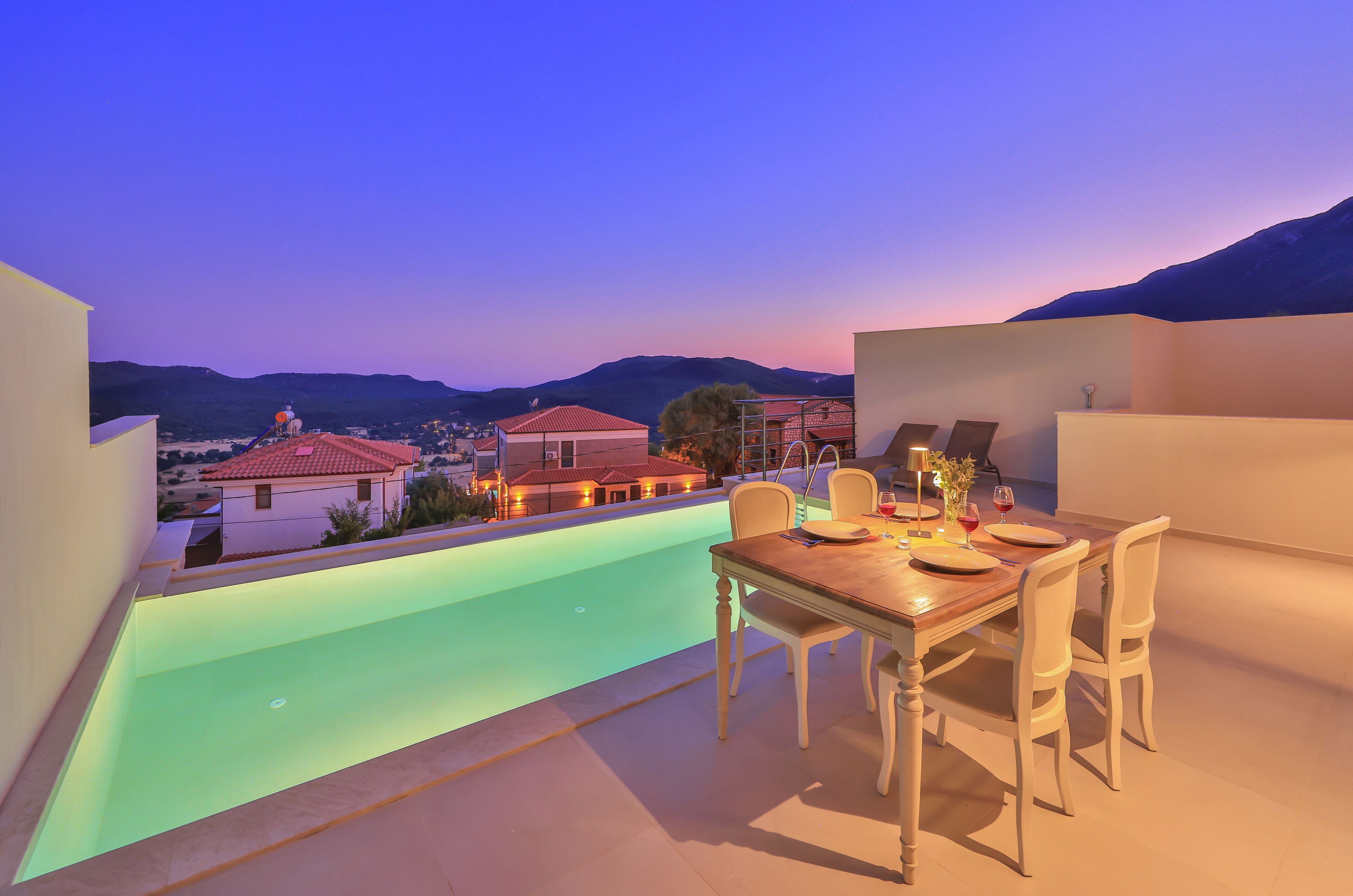 A rooftop terrace with a pool, dining table, and chairs, overlooking a mountainous landscape.