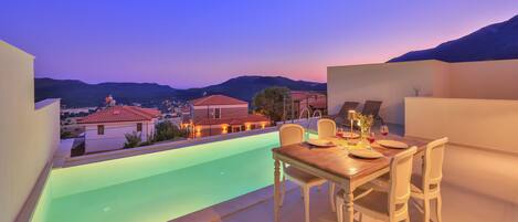 A rooftop terrace with a pool, dining table, and chairs, overlooking a mountainous landscape.