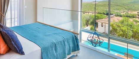 Quarto com cama, vista para uma piscina e uma cadeira suspensa.