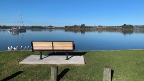 Un banc au bord d’un lac paisible, avec un voilier et un pont en arrière-plan.