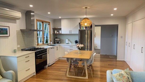 Une cuisine moderne avec des meubles blancs, un réfrigérateur en acier inoxydable et un coin repas comprenant une table et des chaises en bois.