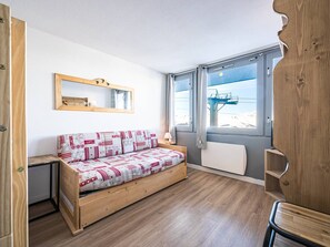 Une petite pièce chaleureuse, avec un canapé en bois, une petite table de chevet, un miroir et une fenêtre donnant sur un télésiège.