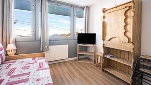 A hotel room with a bed, a TV on a wooden stand, a window with curtains, and a wooden wardrobe.