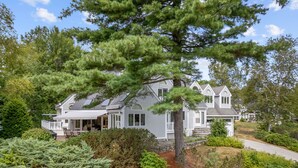Une maison à deux étages avec un patio couvert et un grand arbre à l’avant.