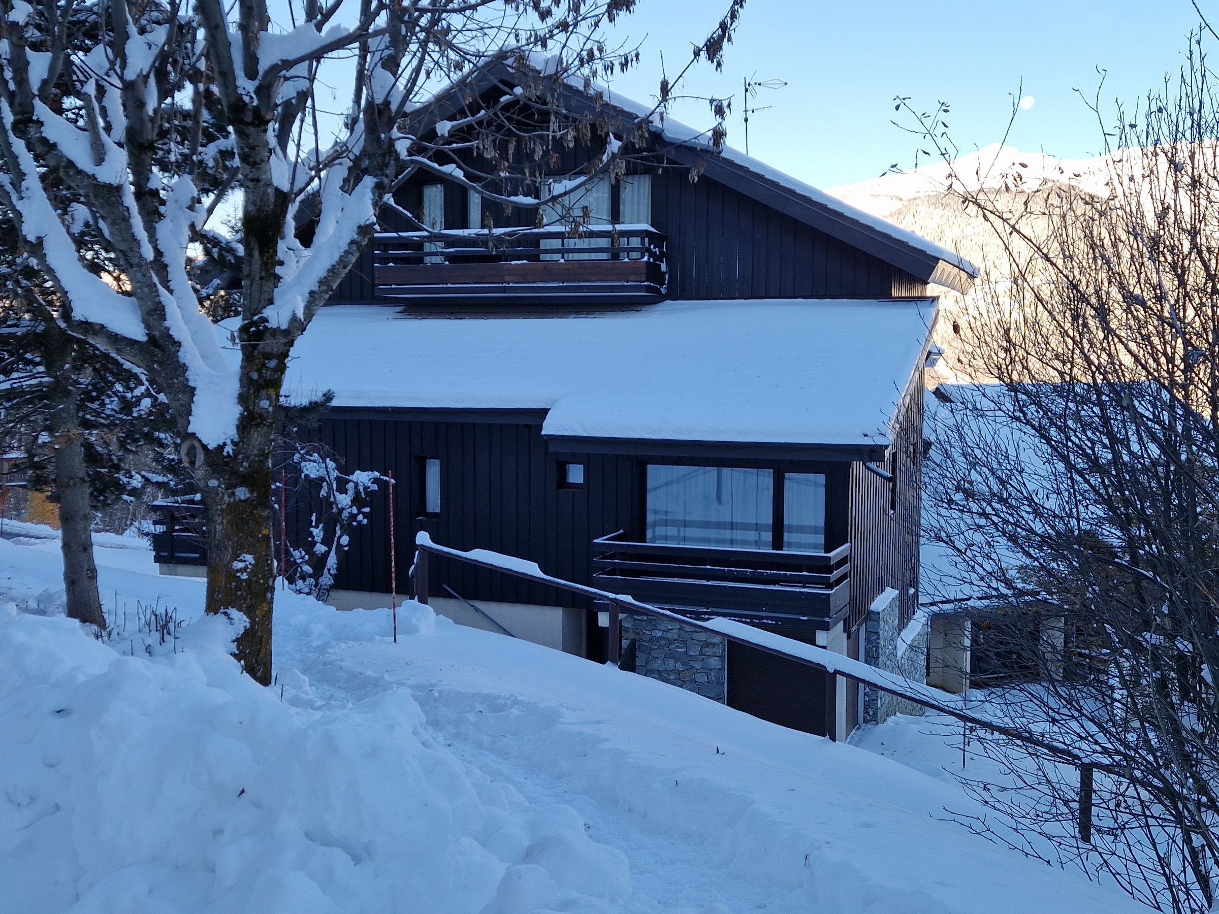 Eine zweistöckige Chalet-Hütte mit Skilift, umgeben von schneebedeckten Bäumen und Bergen.