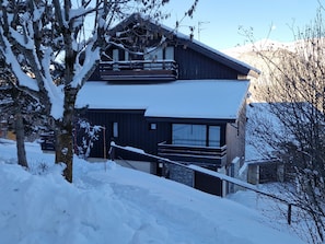 Eine zweistöckige Chalet-Hütte mit Skilift, umgeben von schneebedeckten Bäumen und Bergen.