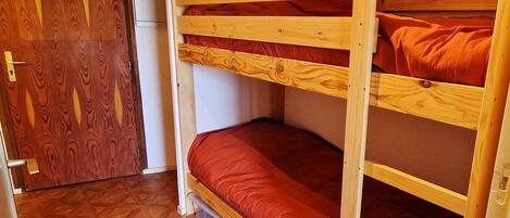 Un lit superposé avec un matelas rouge, dans une pièce dont le sol et la porte sont en bois.