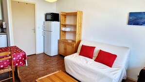 A compact living space with a white sofa, red cushions, a wooden table, a white refrigerator, and a wooden cabinet.