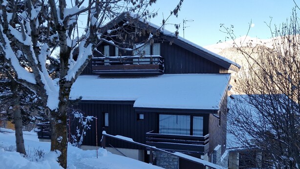 A two-story chalet with a ski lift, surrounded by snow-covered trees and mountains.
