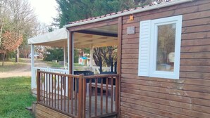 A wooden cabin with a covered porch, a small deck, and a window with shutters. - Mobile Home 34m² with Terrace for 6 in Dévillac (Dévillac)