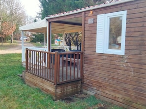 Eine Holzhütte mit überdachter Veranda, einer kleinen Terrasse und einem Fenster mit Fensterläden.