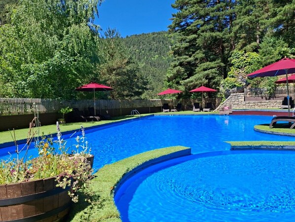 A swimming pool with a wooden deck, surrounded by trees and red umbrellas.
