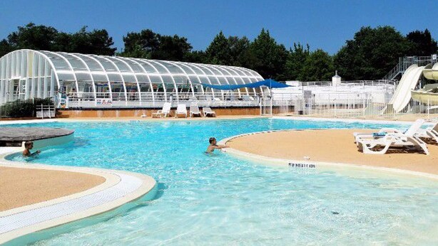 A swimming pool with a glass structure in the background, a sandy beach area, and a water slide. - Prestige Mobile Home with Terrace - 4 people, 2 bedrooms (Soustons)