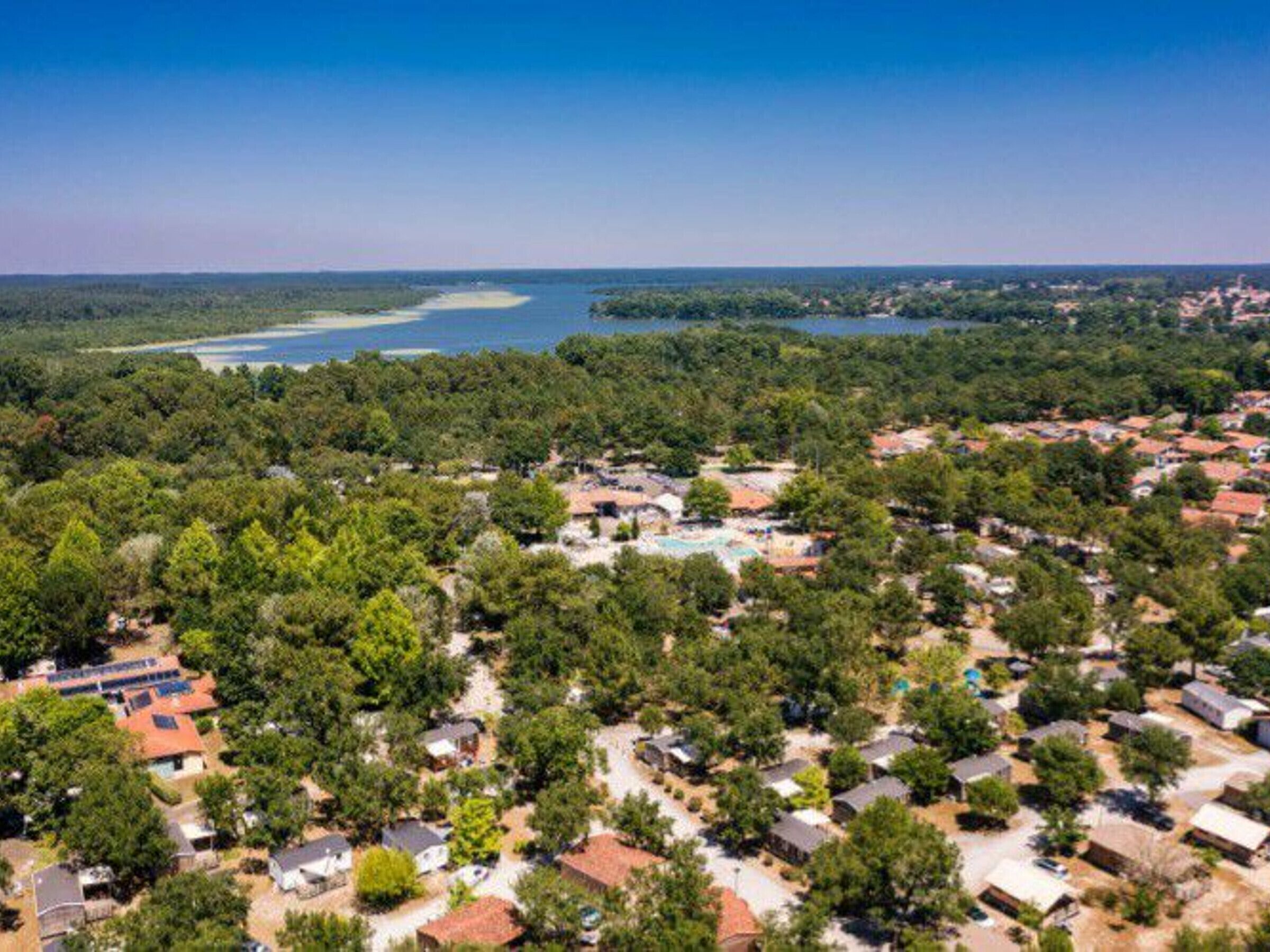 An aerial view of a residential area with houses, a swimming pool, and a lake in the background.
