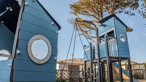 A blue play structure with slides and climbing elements, surrounded by trees and a clear sky. - Mobile home - Terrace for 4 people in Saint-Michel-Chef-Chef (Saint-Michel-Chef-Chef)