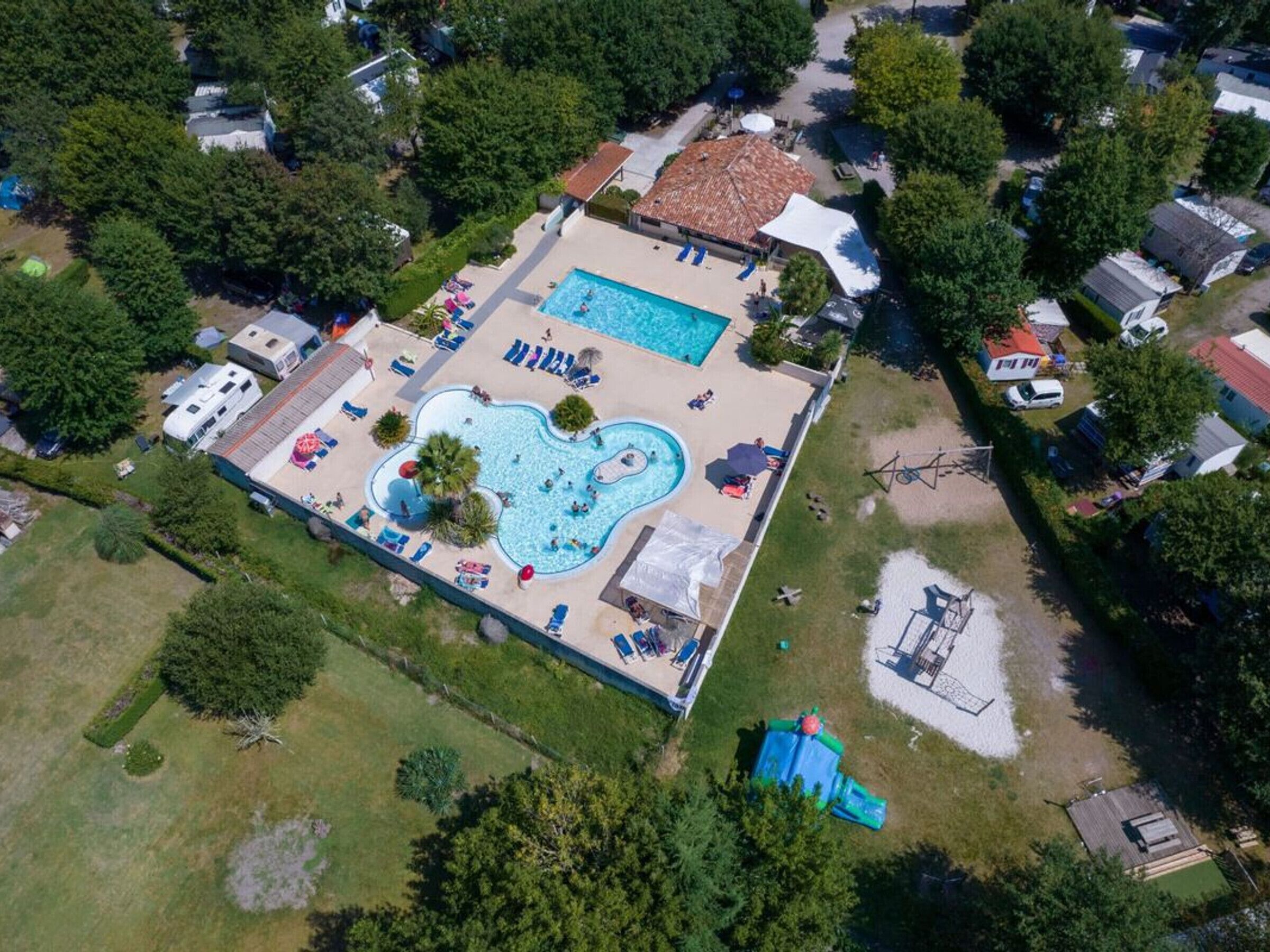 Vue aérienne d’un quartier résidentiel avec une piscine, un petit bâtiment doté d’un toit rouge et plusieurs véhicules stationnés.