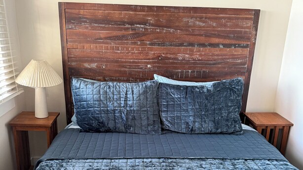 A bed with a wooden headboard, two pillows, and a textured blue bedspread.