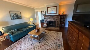 A living room with a blue sofa, a coffee table, a fireplace, a television, and a patterned rug.