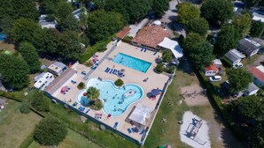 An aerial view of a residential area with a swimming pool, a small building with a red roof, and several parked vehicles.
