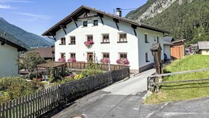 Ein zweistöckiges Gebäude mit Satteldach, zahlreichen Fenstern und einer hölzernen Einfriedung davor.