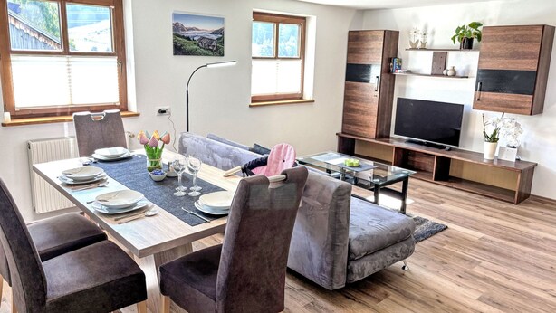 Ein modernes Wohnzimmer mit Essbereich, Holzboden, einem grauen Sofa, einem Flachbildfernseher und einem angebrachten Schrank.