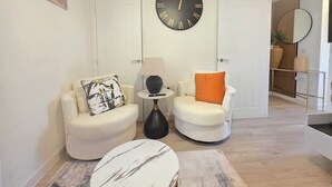 A modern living room with two white armchairs, a round table, and a large wall clock. - Spacious| Modern House |Close to Sites, beach,|Contractors,  families welcome (Yeovil)