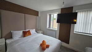 A bedroom with a bed, a nightstand, a mirror, a window with blinds, and a flat-screen TV mounted on the wall. - Spacious| Modern House |Close to Sites, beach,|Contractors,  families welcome (Yeovil)