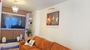 A living room with a large flat-screen TV, a brown sofa, a small table, and a plant. - Spacious| Modern House |Close to Sites, beach,|Contractors,  families welcome (Yeovil)
