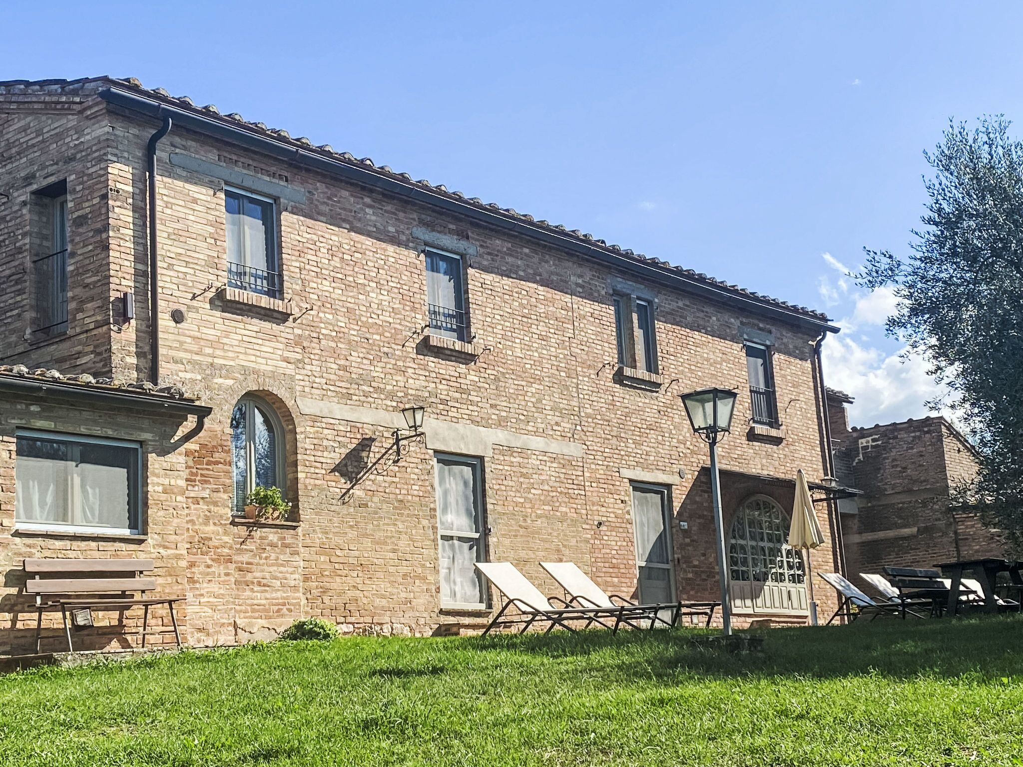 A brick building with multiple windows, a door, and a small garden area with outdoor furniture.